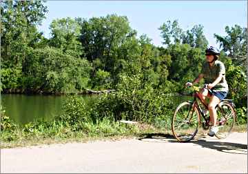 A bicyclist rides along the Red Cedar River.