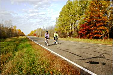 Two bicyclists pedal on the Tour de Cuyuna in fall.