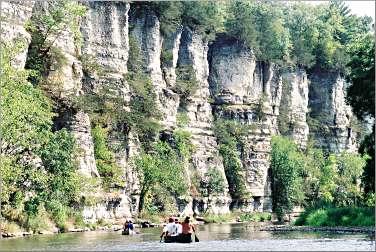 Canoeists paddle at the foot of cliffs on the Upper Iowa.