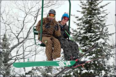 A skier and snowboarder on a chairlift.
