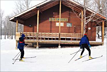 Skiers glide by the Six Swedes cabin at Maplelag.